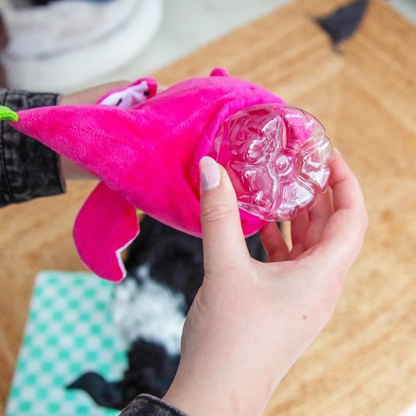 Pink plush toy with a clear plastic container held by a hand on a wooden surface.