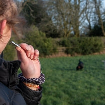 Person using a dog whistle outdoors with a dog in the background