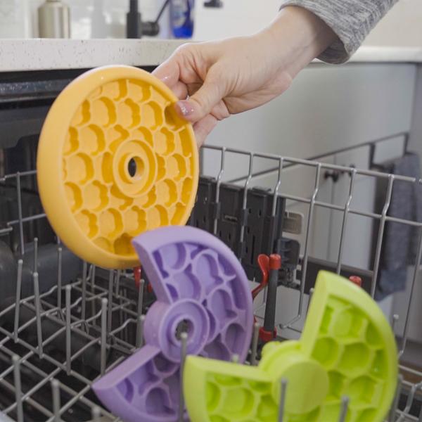 Person holding a Lickin Layers Cat feeder in front of an open dishwasher.