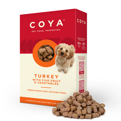 A collection of COYA brand dog food packages in various flavors including chicken, turkey, beef, fish, and pork. The packaging is colorful with images of the food and dogs on it.