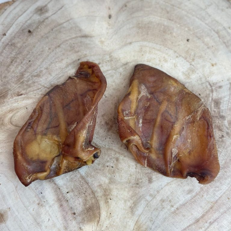 Two large natural pig ear dog chews displayed on a wooden surface, perfect for dental health and chewing satisfaction, all-natural treats from Amy’s Pet Supplies.