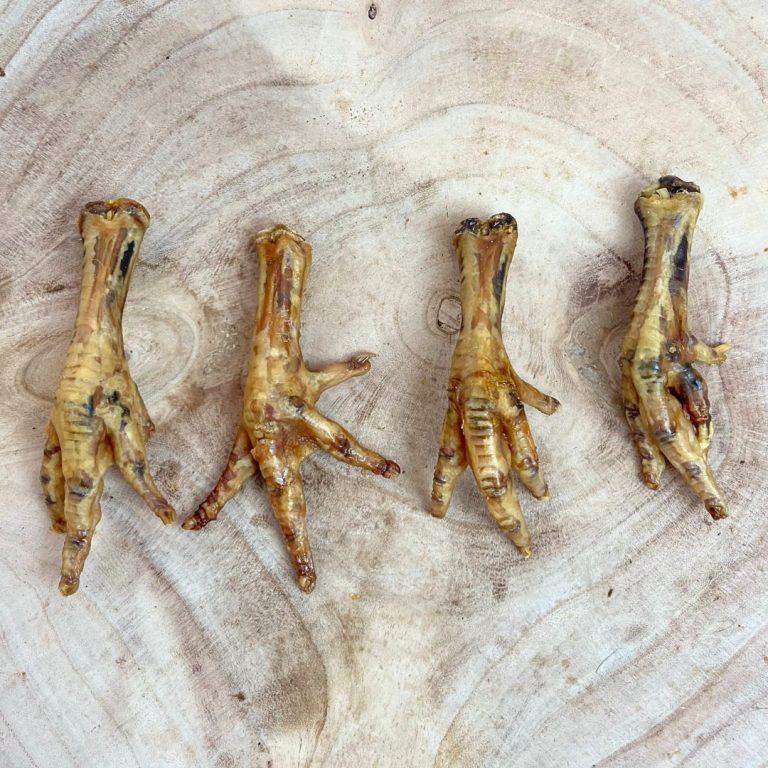 Four air-dried chicken feet dog treats displayed on a wooden surface, natural high-protein chews rich in glucosamine for joint support, available at Amy’s Pet Supplies