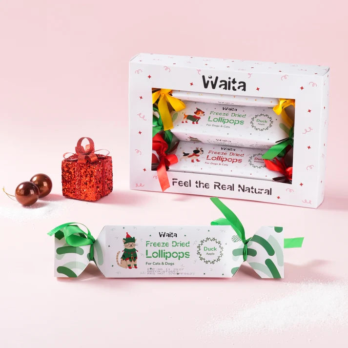 Waita Christmas Cracker Gift Box with wrapped lollipop crackers and coloured ribbons, plus a green cracker displayed in front on a pink background.