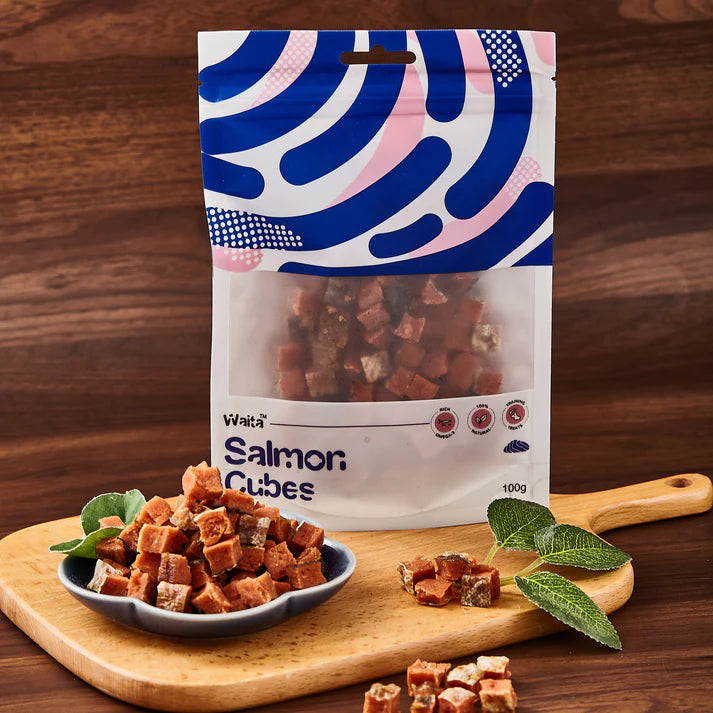 Packaging of Waita Salmon Cubes on a wooden board with salmon cubes and leaves.