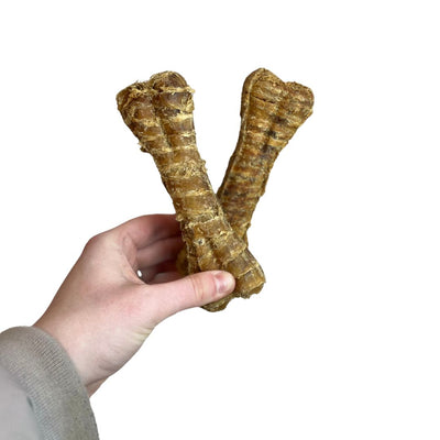Hand holding two large brown dog chew toys against a white background