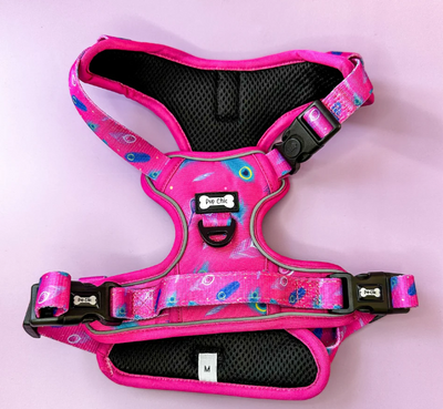 Pup chic Boutique Peacock Power Dog harness on a pastel background. Harness is a fuschia pink with blue peacock Feather Deasign. 